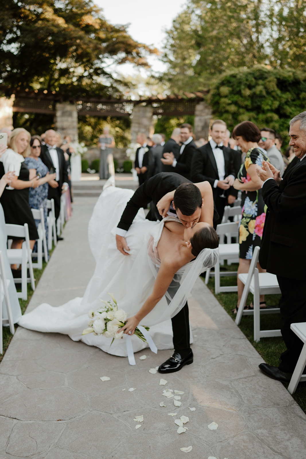 Groom dipping and kissing the bride on the ceremony aisle while guests cheer during the recessional.